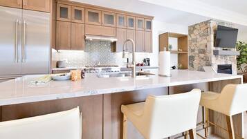 A modern kitchen with a central island, bar stools, a stone fireplace, and a TV mounted above it.