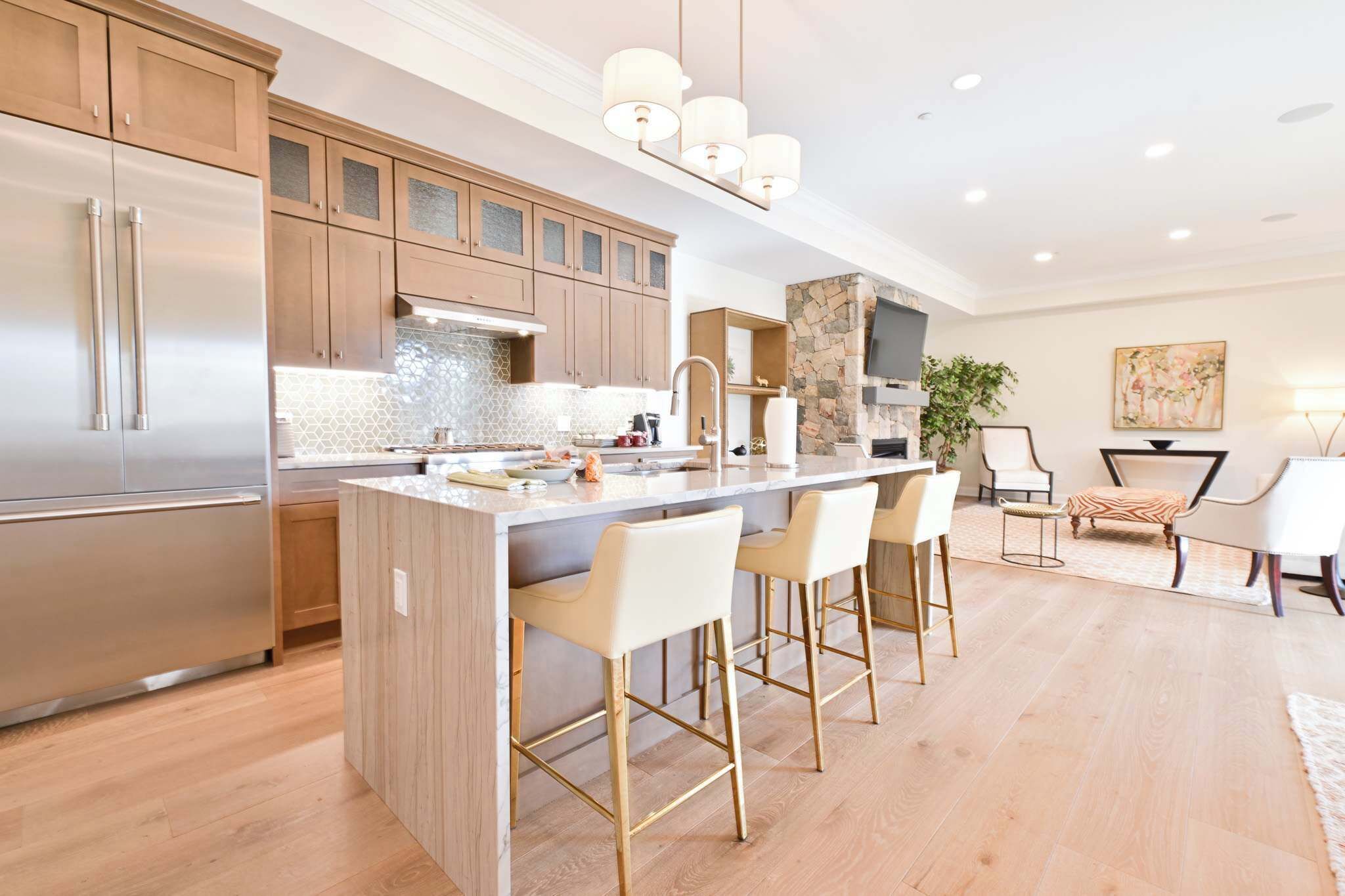 A modern kitchen with a central island, bar stools, and a stone accent wall.