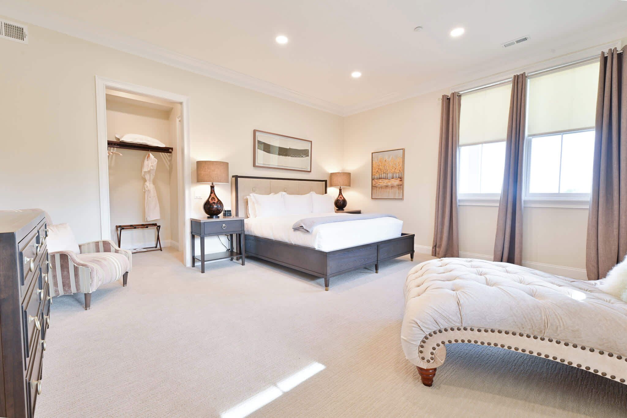 A bedroom with a bed, bedside tables, a dresser, a walk-in closet, and a window with curtains.