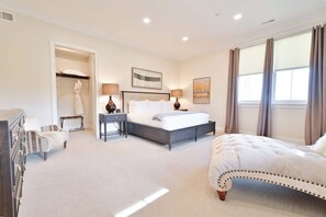 A bedroom with a bed, bedside tables, a dresser, a walk-in closet, and a window with curtains. - Hilltop | Village Two Bedroom Suite (Richmond)