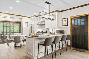 A modern kitchen with a central island, bar stools, and a black door.