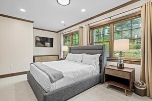 A bedroom with a bed, bedside tables, a TV, and large windows with curtains.
