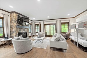 A spacious living room with a stone fireplace, comfortable seating, and large windows.