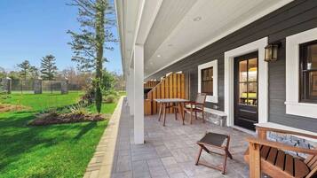A covered patio with outdoor furniture, a stone pathway, and a view of a grassy area.