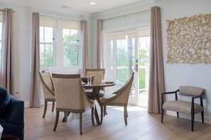 A dining area with a round table and chairs, large windows, and a view of greenery outside.