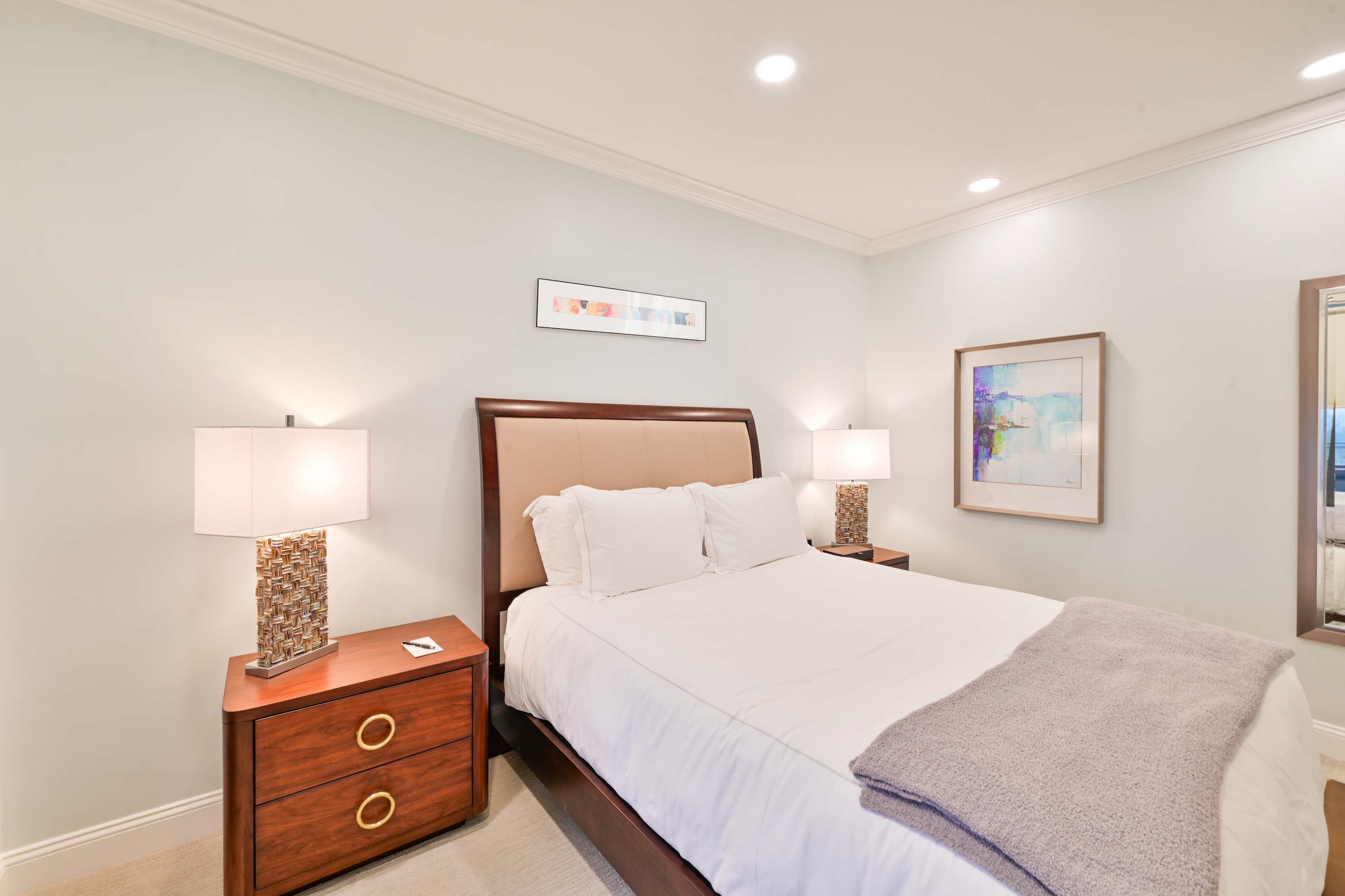A hotel room with a bed, two bedside tables, a nightstand, a drawer unit, and a wall-mounted picture.