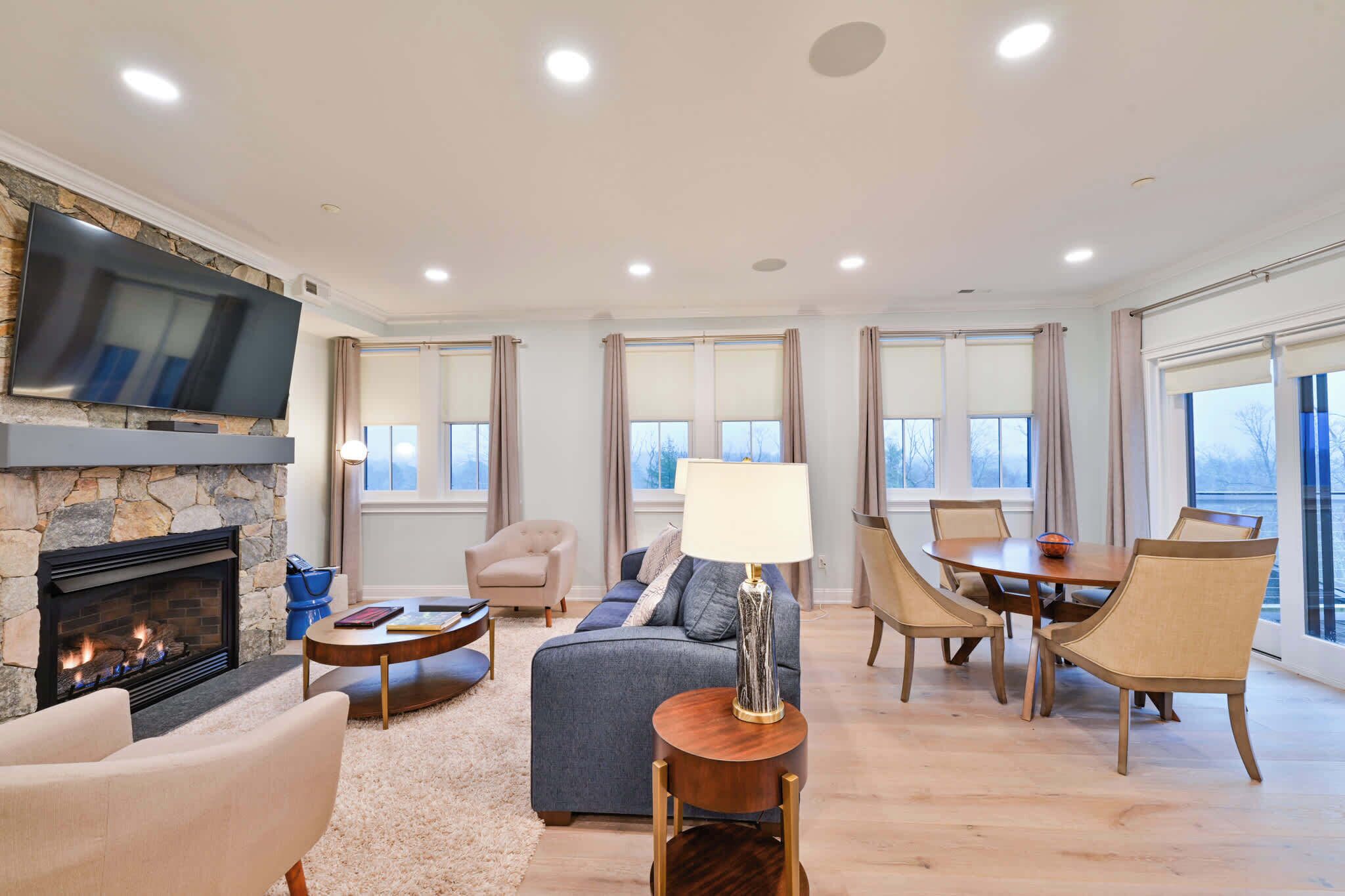 A spacious living room with a fireplace, a television mounted on a stone wall, and a dining area with a table and chairs.