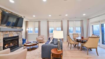 A spacious living room with a fireplace, a television mounted on a stone wall, and a dining area with a table and chairs.