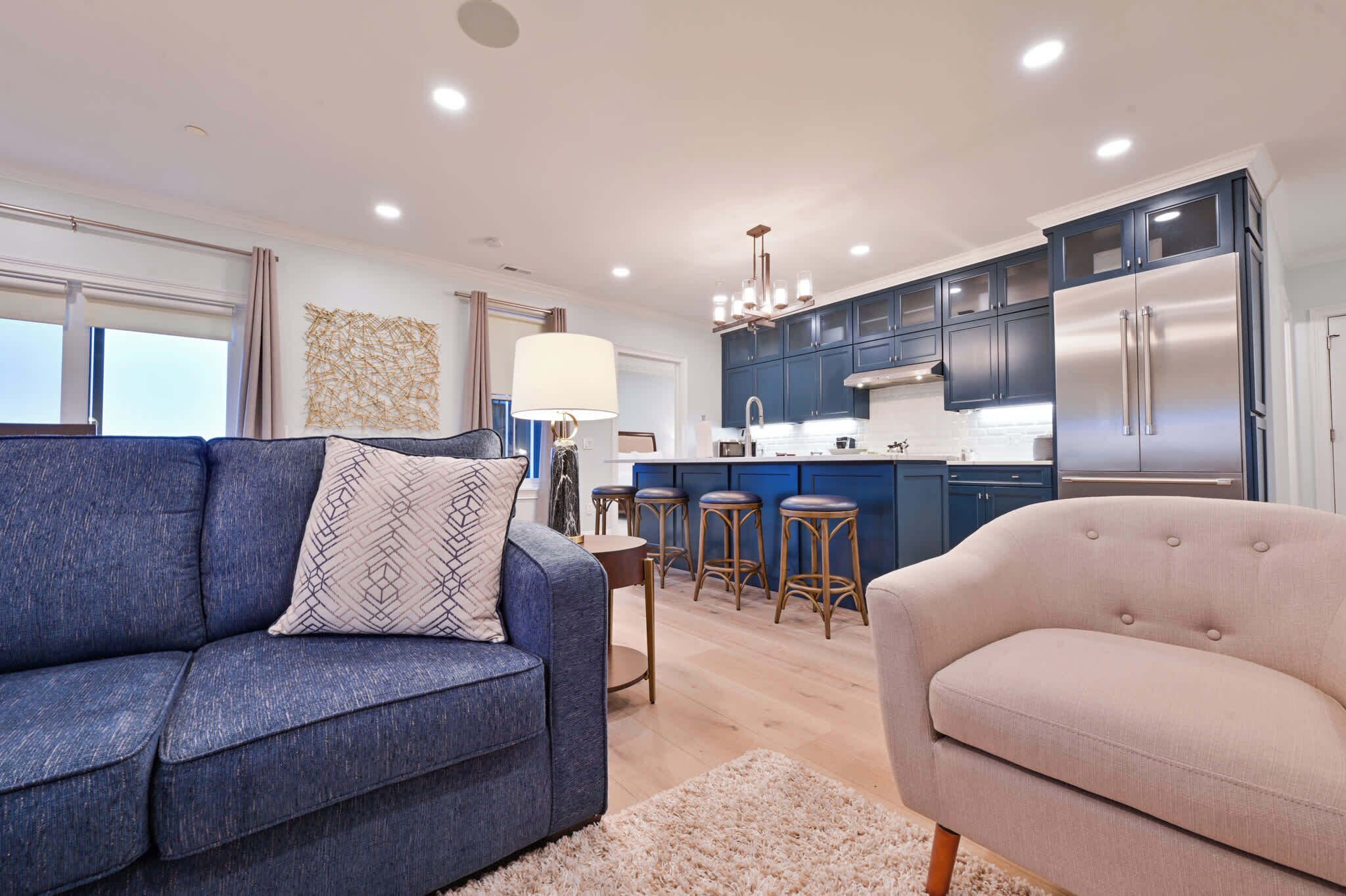 A modern kitchen with dark blue cabinets, a stainless steel refrigerator, and a central island with stools.