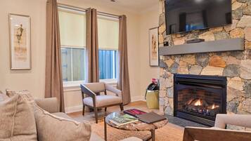 A living room with a stone fireplace, a flat-screen TV mounted on the wall, a sofa, and a coffee table.