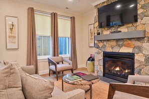 A living room with a stone fireplace, a flat-screen TV mounted on the wall, a sofa, and a coffee table. - Hilltop | Woodland Suite (Richmond)