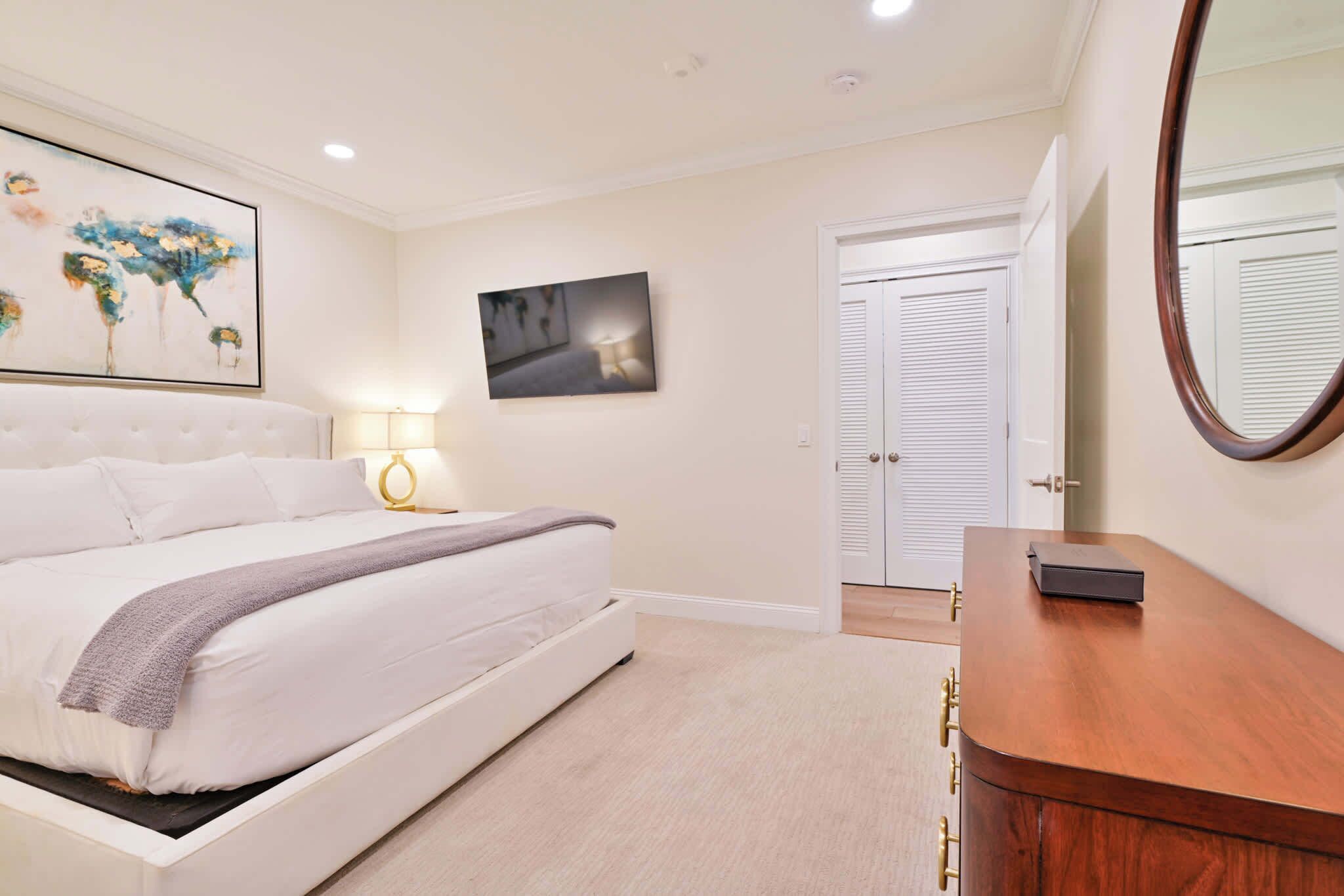 A bedroom with a bed, bedside table, lamp, and artwork on the wall.