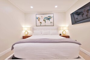 A bedroom with a large bed, two bedside lamps, a framed artwork above the bed, and a small table with a lamp.