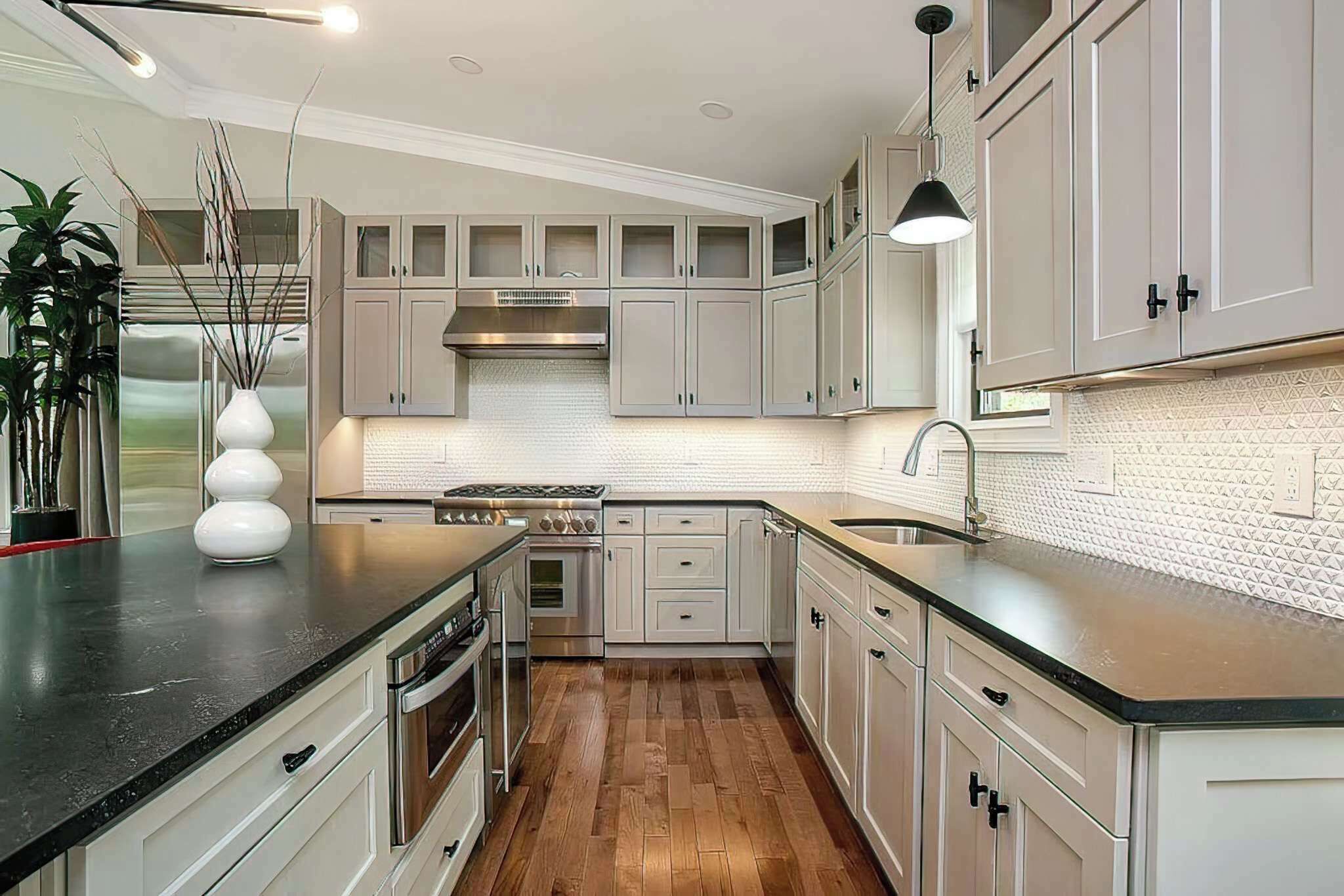 A modern kitchen with white cabinets, a black countertop, and a stainless steel range hood.