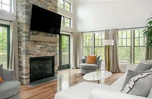 A spacious living room with a stone fireplace, comfortable seating, large windows, and a modern design.