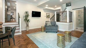 Un salon spacieux avec un canapé gris, un téléviseur à écran plat, un escalier et un coin repas comprenant une table et des chaises.
