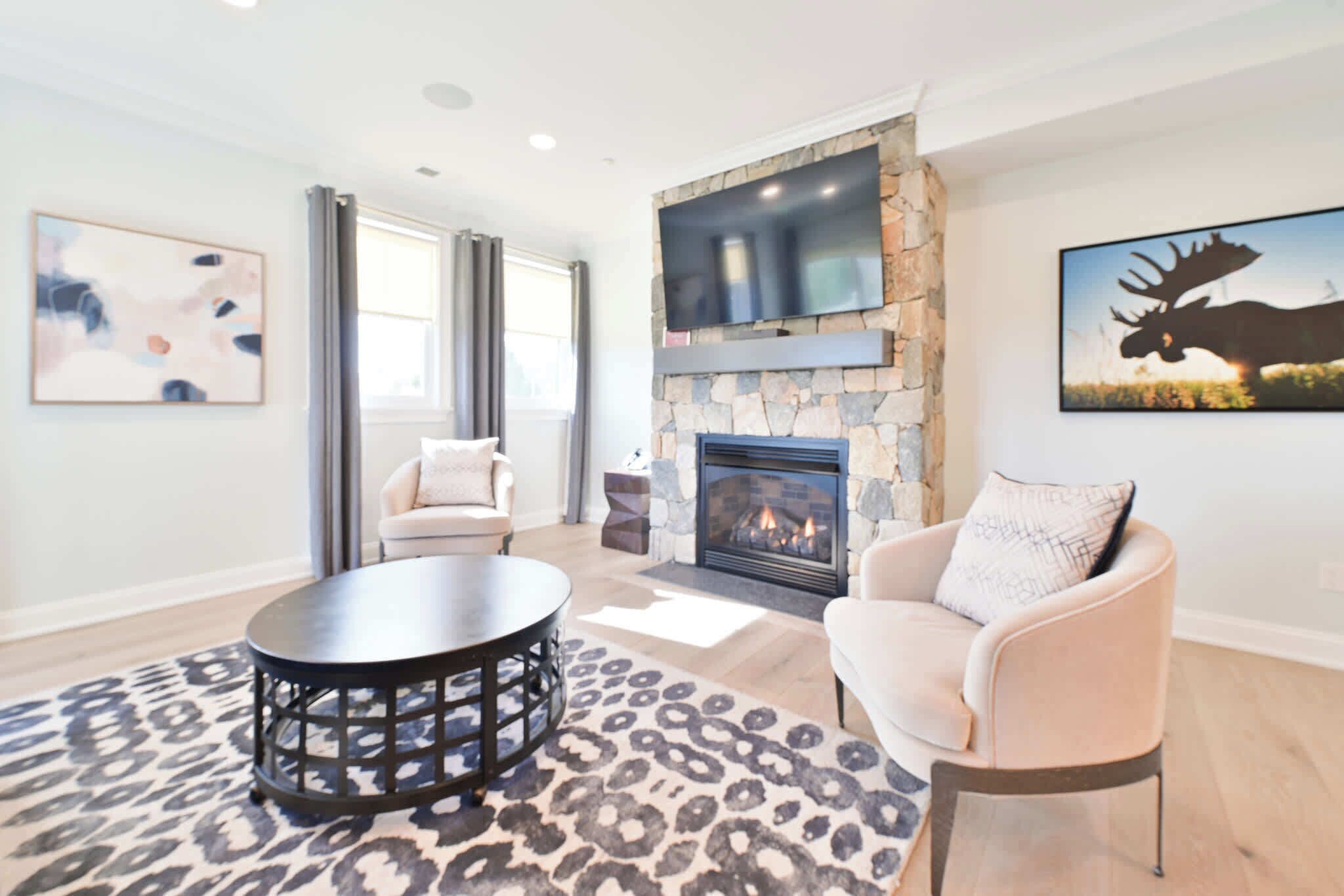 A modern living room with a stone fireplace, a mounted TV, and a large moose painting.