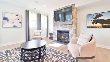 A modern living room with a stone fireplace, a mounted TV, and a large moose painting.