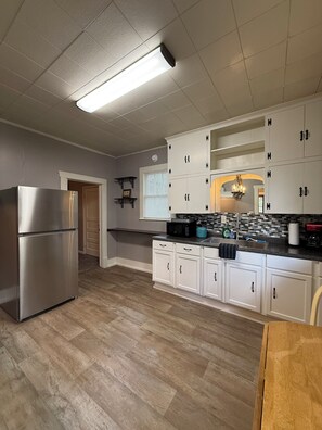A kitchen with white cabinets, a stainless steel refrigerator, and a wooden floor.