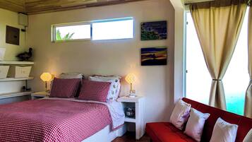 A bedroom with a bed, bedside tables, a red sofa, a window, and wall art.