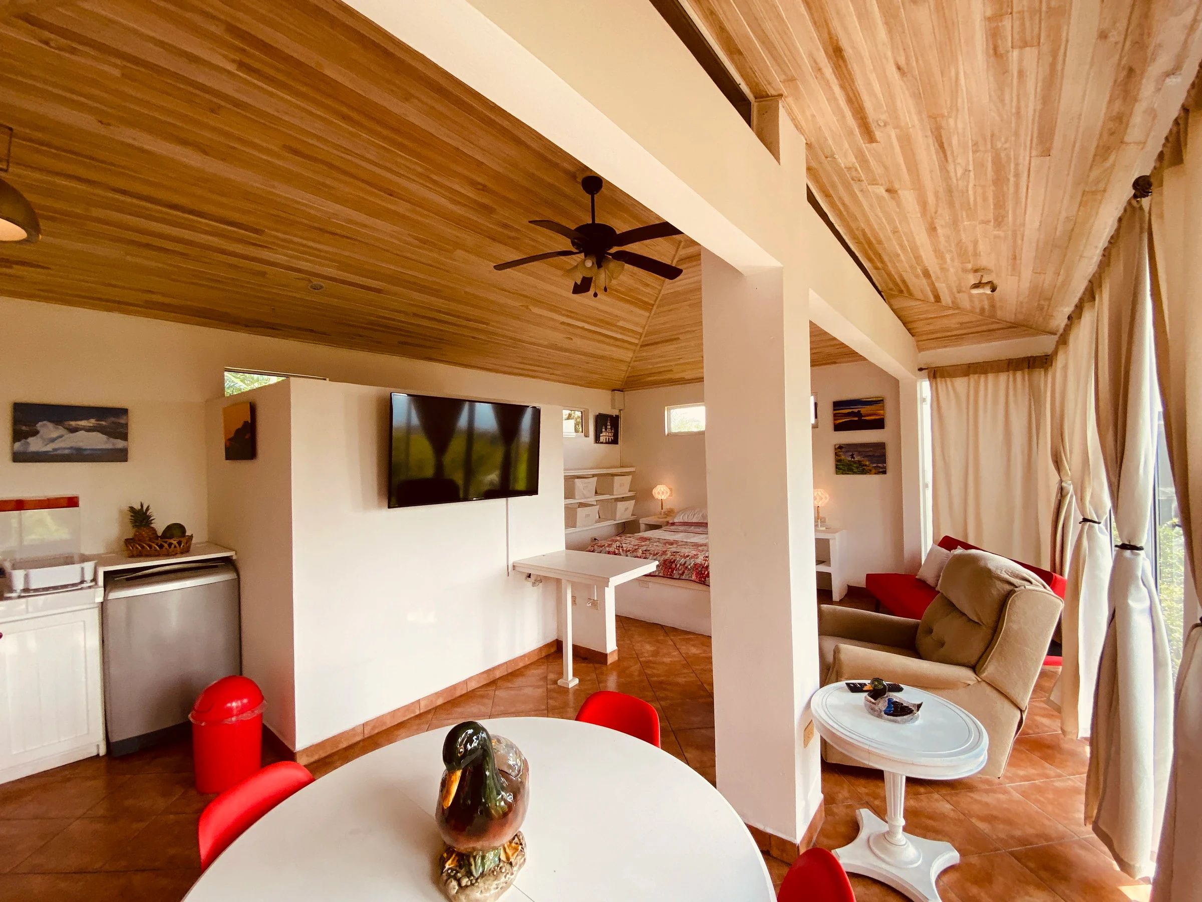 Un vaste espace de vie doté d’un ventilateur de plafond, d’un téléviseur à écran plat fixé au mur, d’une table à manger avec des chaises, et d’un coin salon confortable avec un canapé et des fauteuils.