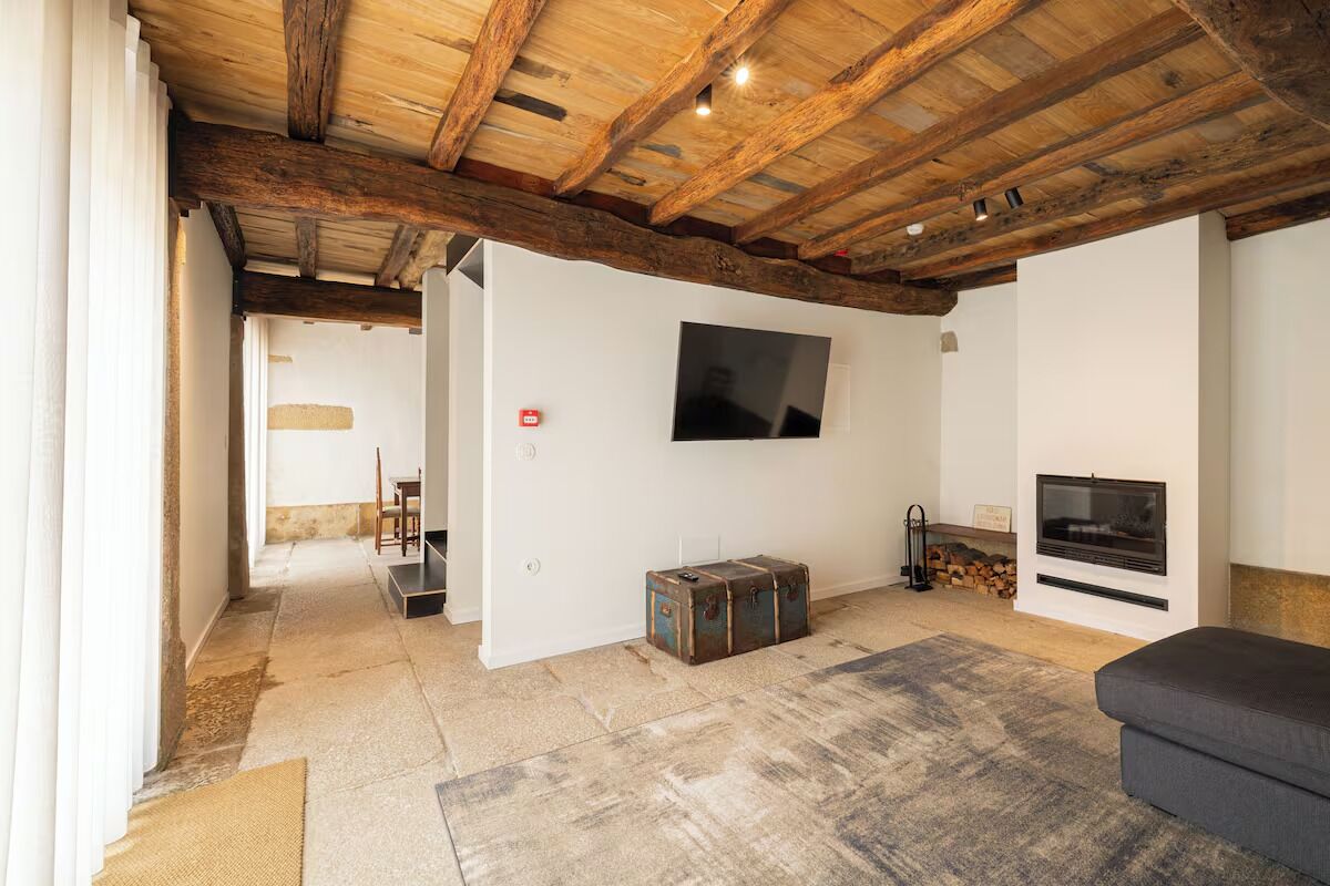 Un salón amplio con vigas de madera a la vista, un televisor de pantalla plana montado en la pared, una chimenea y una zona de estar acogedora.