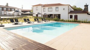 A swimming pool with lounge chairs and umbrellas, surrounded by a wooden deck and a white building with a tiled roof. - Peaceful Farmhouse Stay in Parada de Tibães Portugal Surrounded by Nature (Braga)