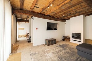 A spacious living room with exposed wooden beams, a flat-screen TV mounted on the wall, a fireplace, and a cozy seating area.