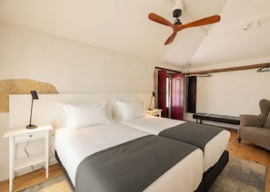 Una camera da letto con due letti, un ventilatore a soffitto, un comodino, una sedia e una porta che dà su un'altra stanza.