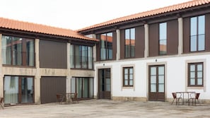 A two-story building with large windows and a tiled roof. There are two doors and a small outdoor seating area with chairs. - Peaceful Farmhouse Stay in Parada de Tibães Portugal Surrounded by Nature (Braga)