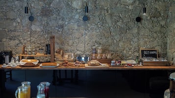 En morgenmadsbuffet med en stenvæg i baggrunden, kaffestation og et skilt med teksten "BEM-VINDOS A CASA NOSTRA".