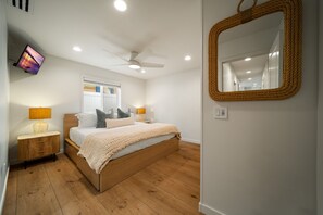 Ein Schlafzimmer mit einem Bett, Nachttischlampen, einem Deckenventilator, einem Fernseher und einem Spiegel.