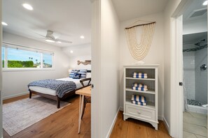 A bedroom with a bed, a desk, a white shelving unit, and a view of the outdoors. - The Famous Big Blue Units 1 & 4 (San Diego)