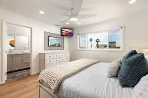 Un dormitorio con cama, ventilador de techo, televisor, ventana con vistas y cómoda.