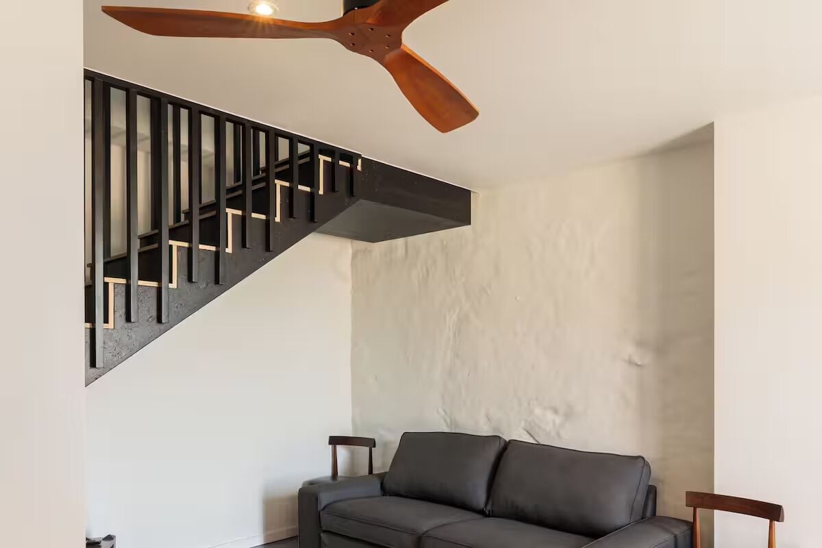 Un interno moderno con una scala nera, una ventola a soffitto e un divano grigio.