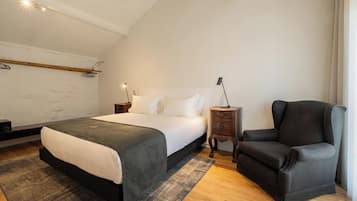 A bedroom with a bed, a chair, a nightstand, and a wall-mounted shelf.