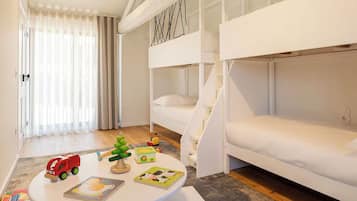 A children's room with bunk beds, a small table with toys and books, and a window with sheer curtains.