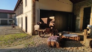 Un edifici rústic amb façana de pedra, un carro de fusta, grans bales de fenc i una zona exterior coberta.