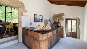 Una cuina rústica amb una illa de fusta, parets de pedra i una finestra gran amb vista a vegetació.