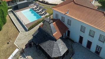 Ovenudblik over en ejendom med swimmingpool, overdækket terrasse og en bygning med tegltag.