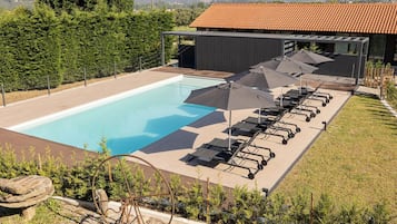 Una piscina amb gandules i ombrel·les, envoltada de vegetació i un edifici amb teulada enrajolada.
