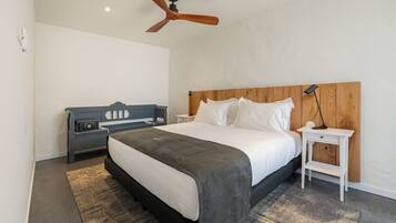 A modern bedroom with a large bed, a wooden headboard, a bedside table with a lamp, and a ceiling fan.
