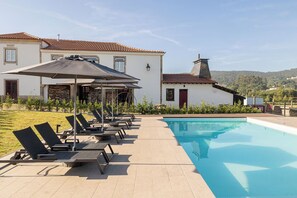 A poolside area with lounge chairs and umbrellas, a swimming pool, and a building with a tiled roof. - Chic Rural Escape with Pool Access and Relaxing Ambience in Parada de Tibães (Braga)