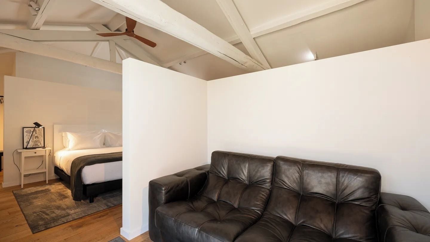 A bedroom with a bed, a nightstand, a black leather sofa, and a ceiling fan.