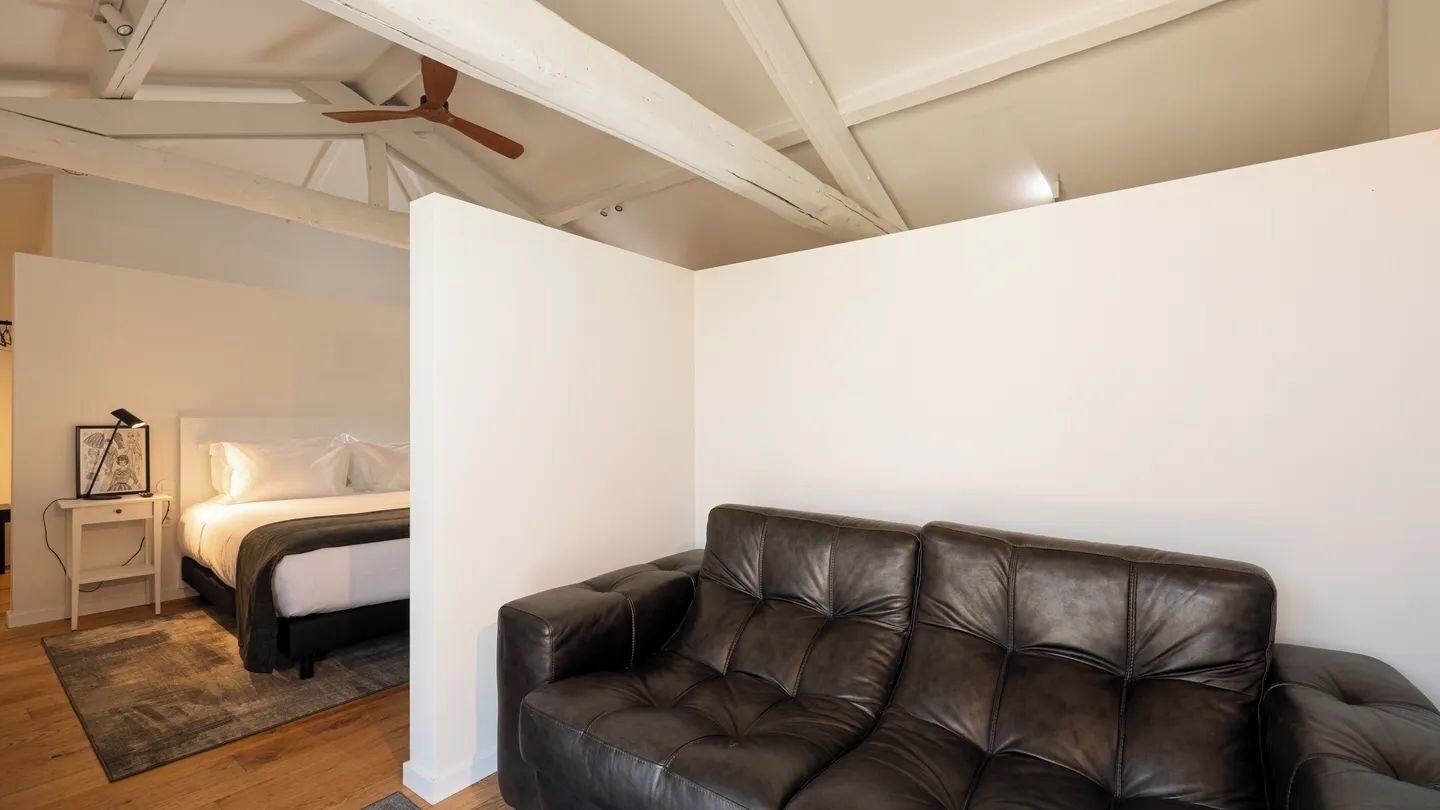 A bedroom with a bed, a nightstand, a black leather sofa, and a ceiling fan.