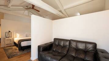 A bedroom with a bed, a nightstand, a black leather sofa, and a ceiling fan.