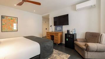 A modern hotel room with a bed, a desk, a chair, a flat-screen TV, and an air conditioning unit.