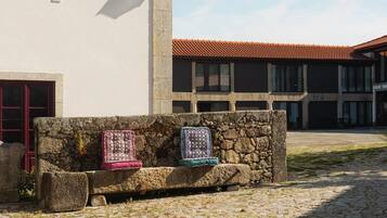 A stone bench with blankets in front of a building with a red-tiled roof and a stone wall.