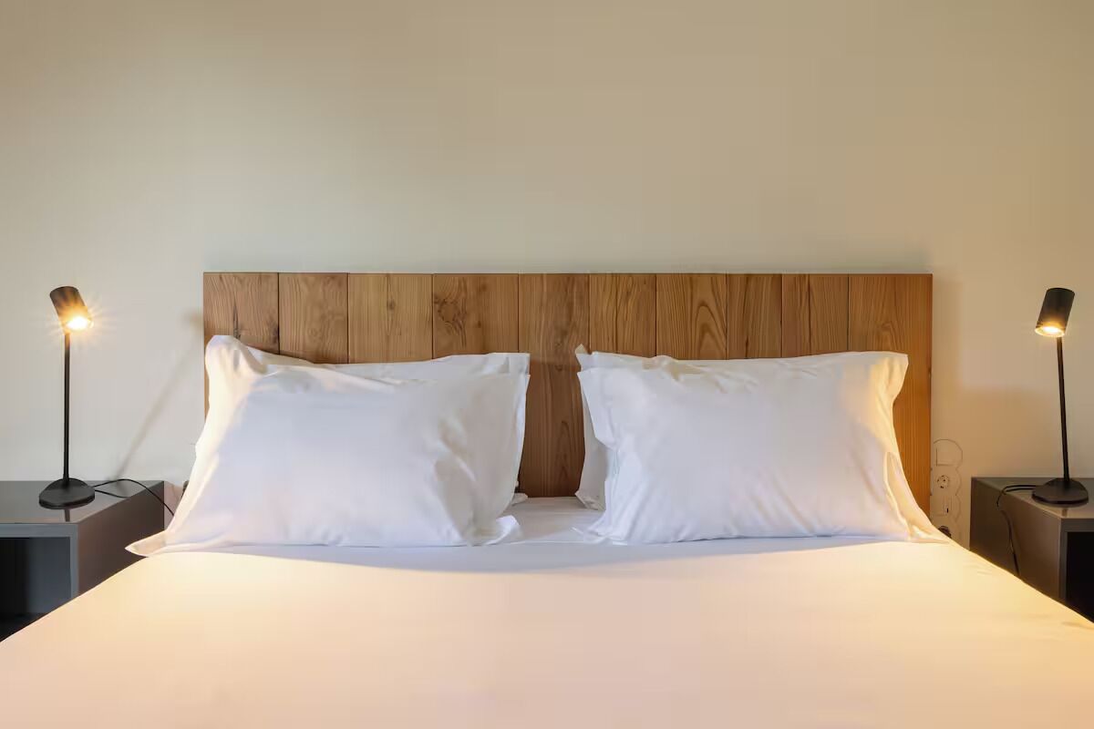 Ein Bett mit Holz-Kopfteil, zwei Nachttische mit Lampen und weißer Bettwäsche.