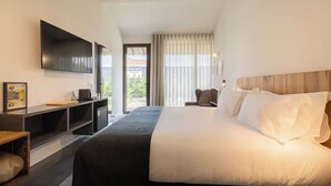 A modern hotel room with a large bed, a flat-screen TV mounted on the wall, a desk with a chair, and a view of the outdoors through a large window. - Romantic Rural Escape with Pool Access and Relaxing Ambience Near Guimarães (Braga)